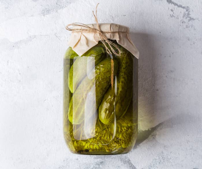 Pickles in a glass jar with dill and garlic on grey table. 
