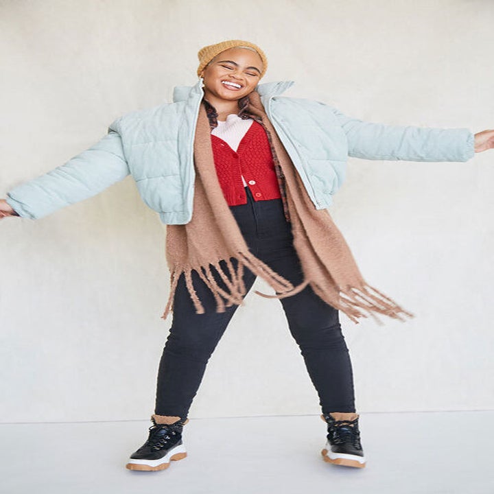 Model wears light blue puffer coat with black jeans and a red cardigan