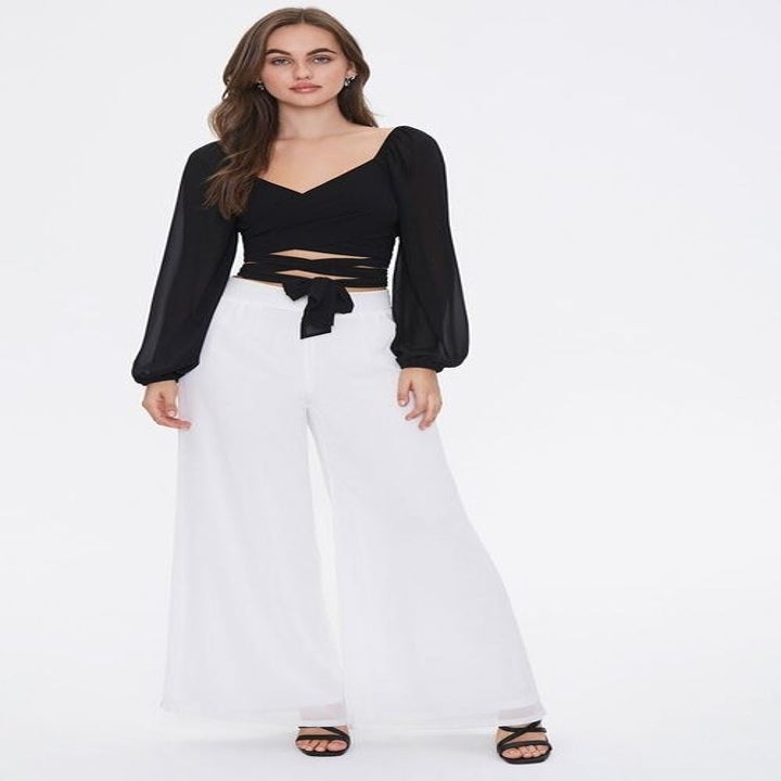 Model wears black wrap peasant top with white flare pants
