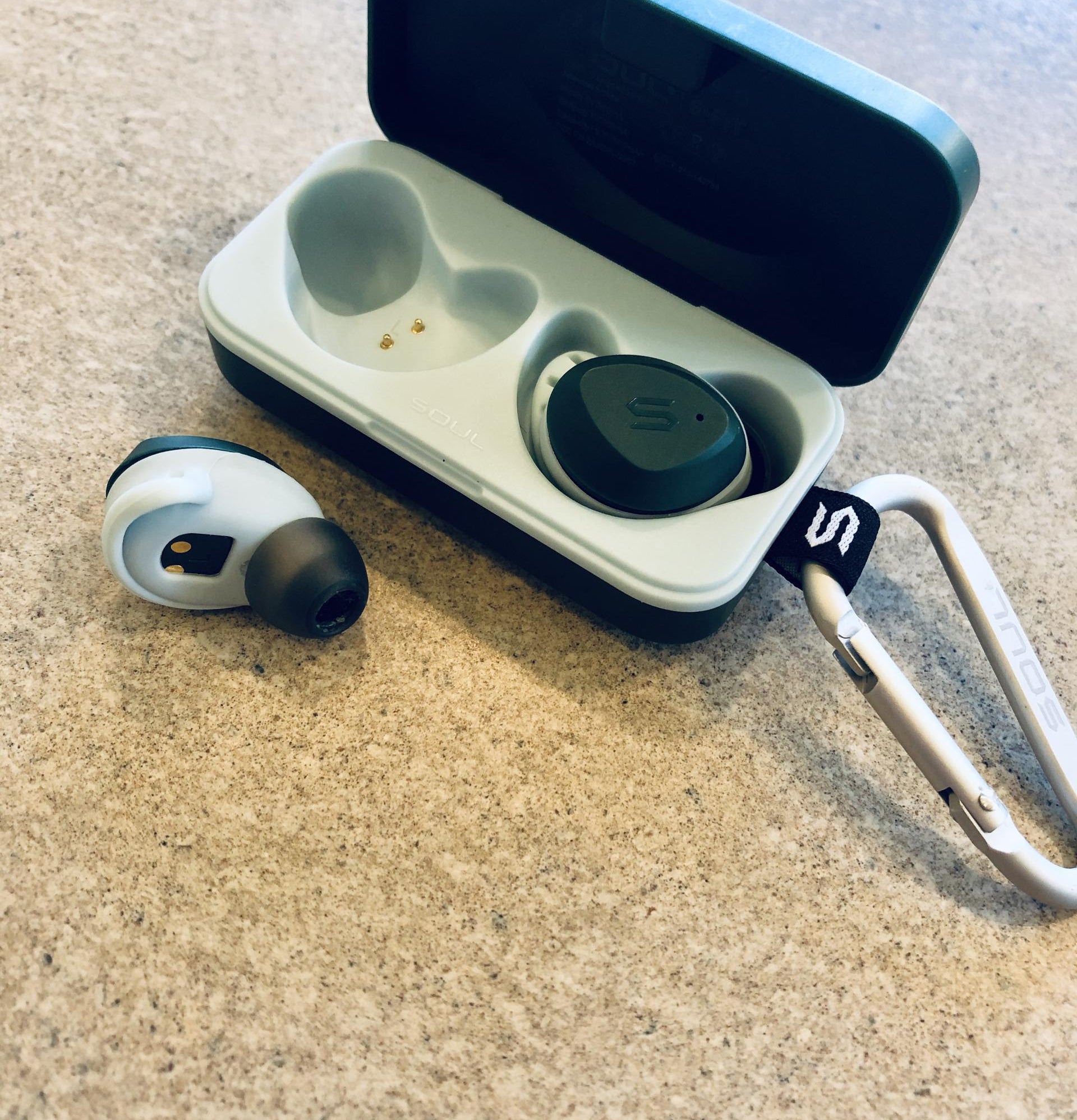 small wireless earbuds in their charging base attached to a carabiner