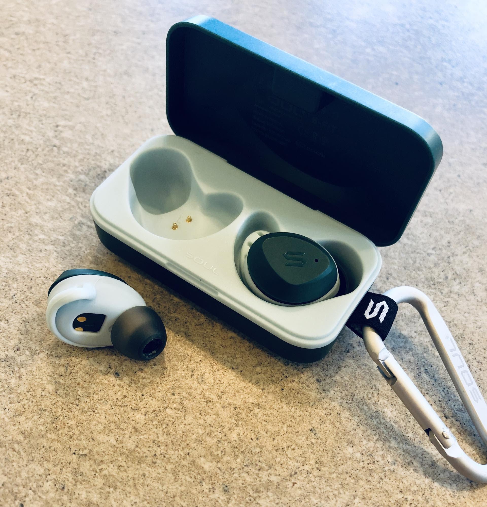 small wireless earbuds in their charging base attached to a carabiner