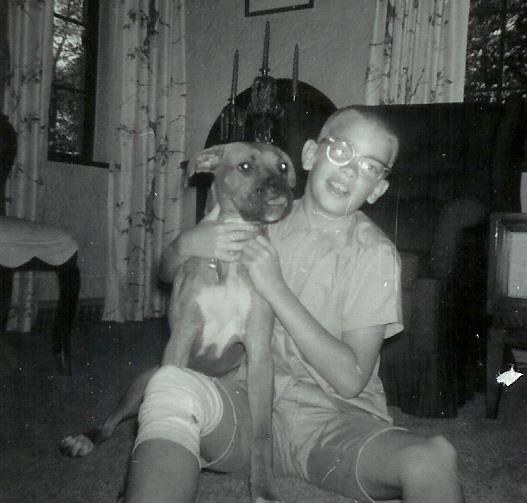 Finefrock as a child wears glasses and sits on the floor smiling and holding his dog, a boxer