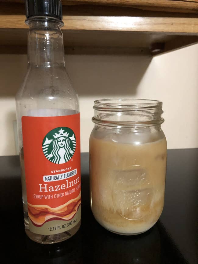 buzzfeed editor showing their coffee next to a bottle of hazelnut syrup