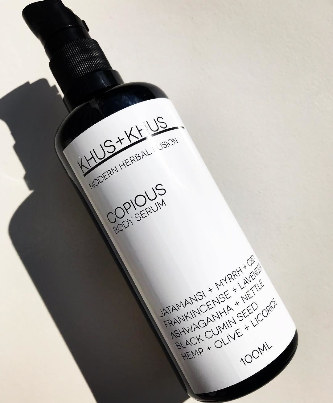 A black pump bottle with a white label of Khus + Khus Copious Body Serum 