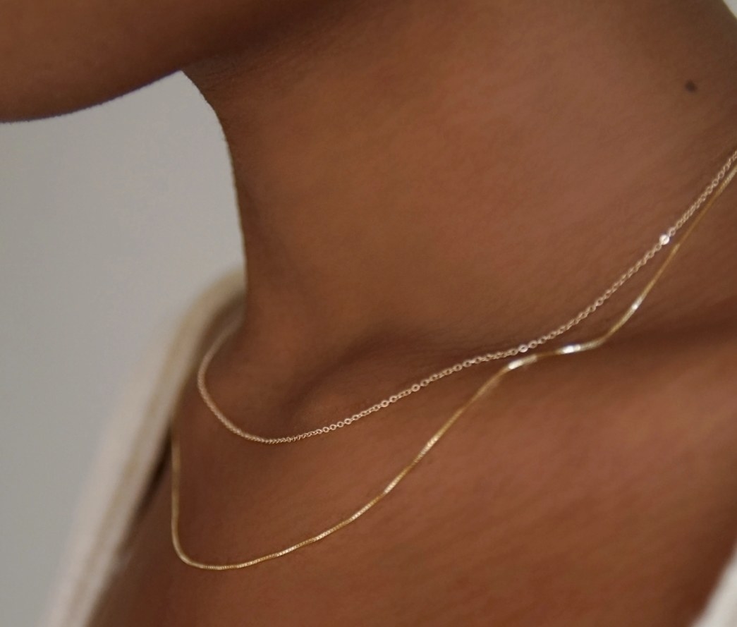 a model wearing two thin gold chains around their neck