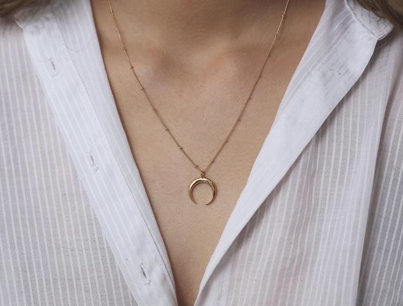 a model wearing a gold moon horn pendant on a gold necklace