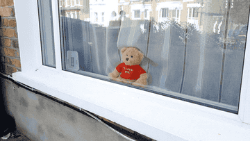 A teddy bear sits inside a window wearing a sweater that reads &quot;I love you&quot;