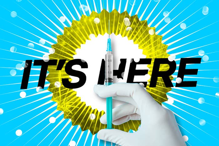 The words "It's here" are in bold behind a gloved hand holding up a syringe