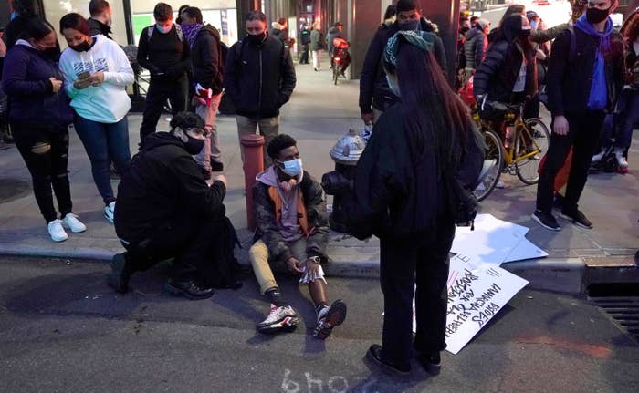 A young man holds his bandaged leg while sitting on the curb