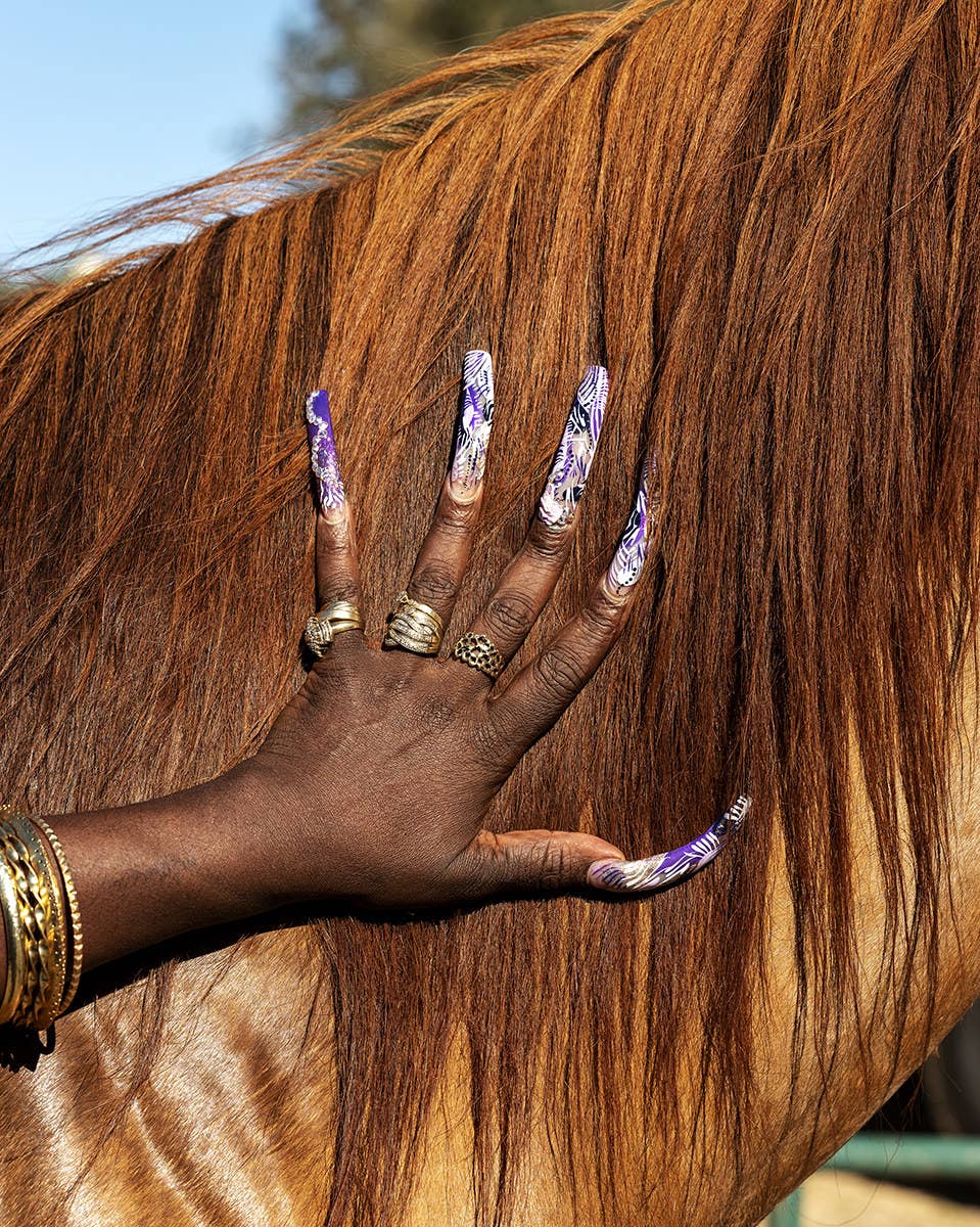 A woman&#x27;s nails with gold jewelry petting a horse