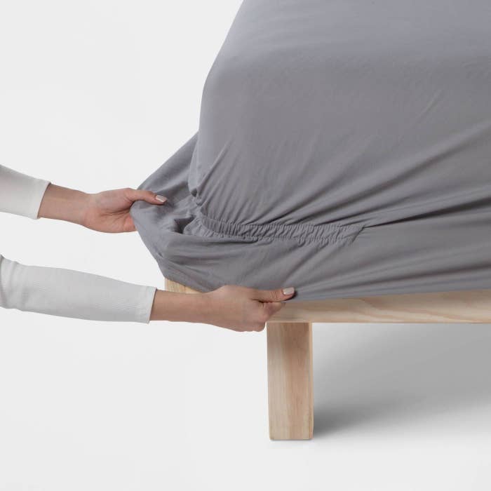 A person pulling the sheet over the corner of a bed