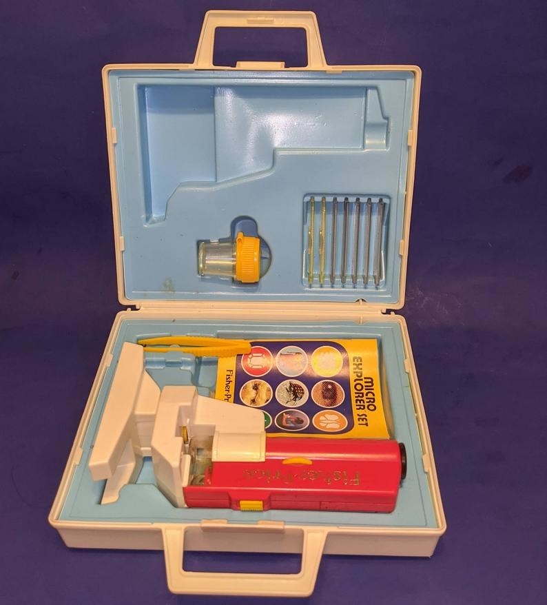 Fisher-Price Micro Explorer Set case open showing a red play microscope and yellow instruction book inside