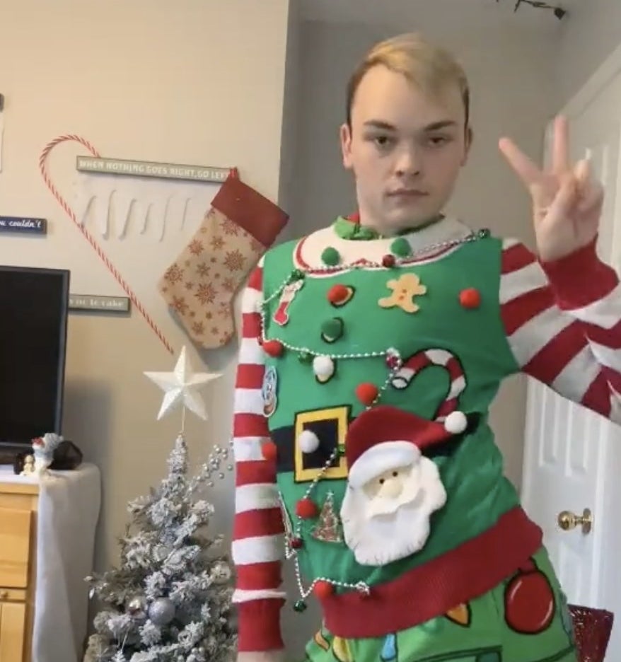 A man flashes a peace sign in a elf sweater