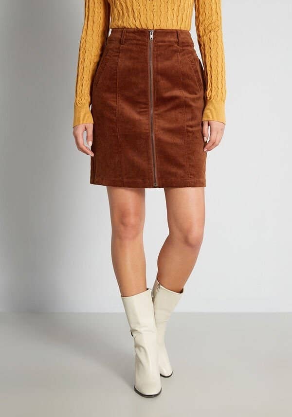 a model wearing the corduroy skirt with white boots and a yellow sweater