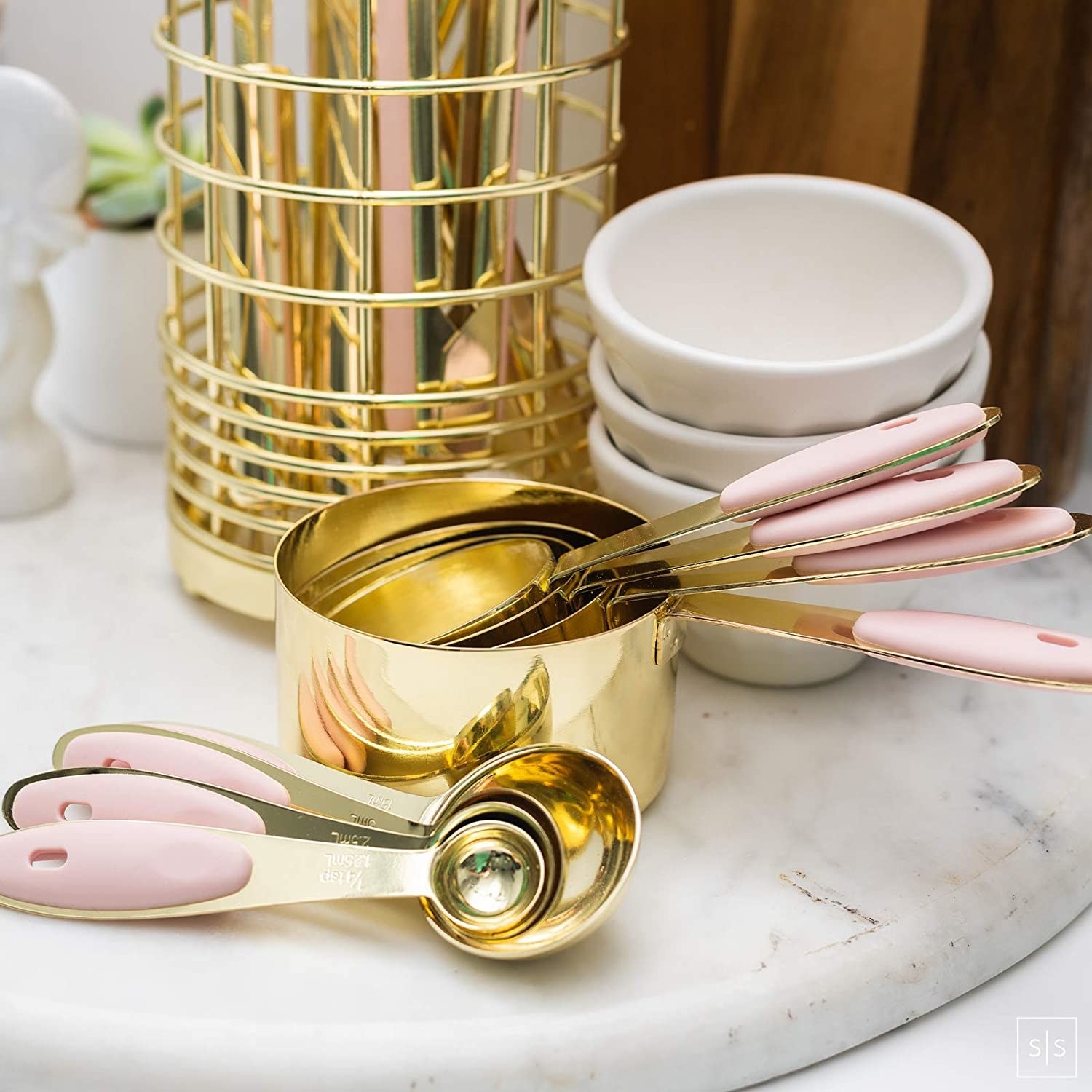 gold tone measuring cups with engraved sizes on them and light pink handles