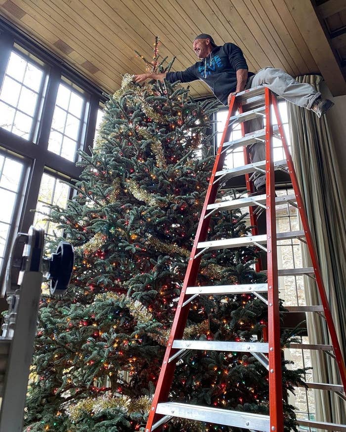 Tim McGraw standing on a ladder, decorating a massive Christmas tree