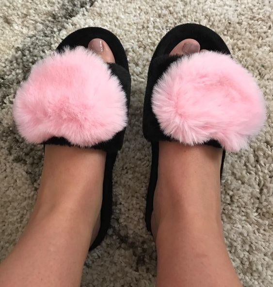 Reviewer wearing the black sandal slippers with big fuzzy hearts