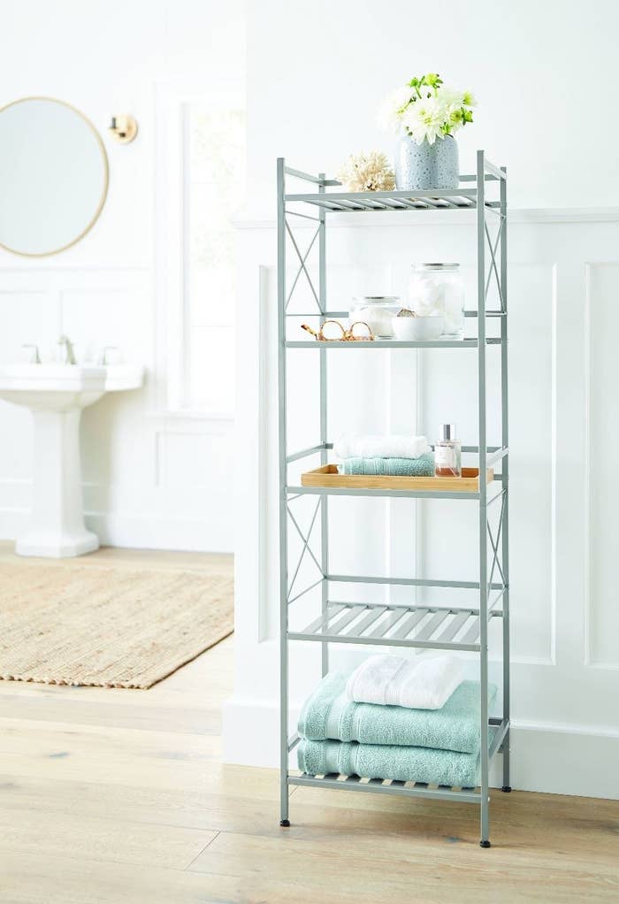 Brushed Nickel shelving unit with aqua and white towels and some bottles displaying cotton balls and flowers
