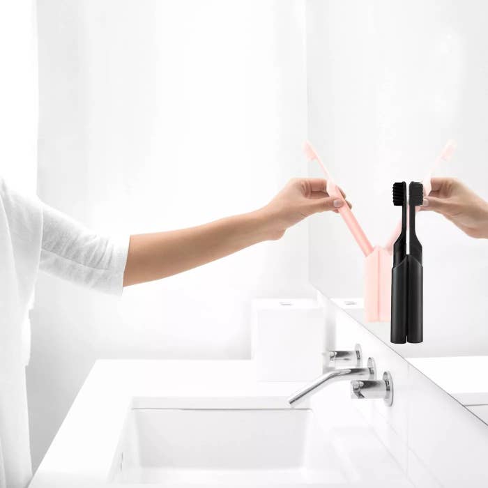 A model removing the pink electric toothbrush from its mirror mount next to the black electric toothbrush