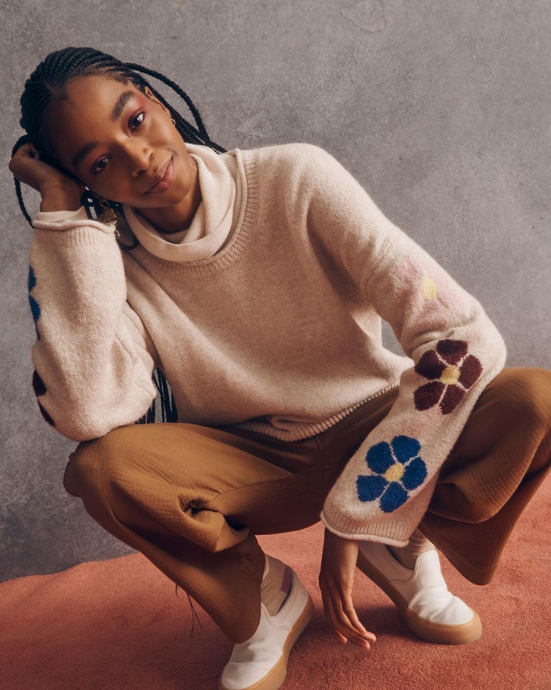 model in brown pants and a tan sweater with flowers on the sleeves
