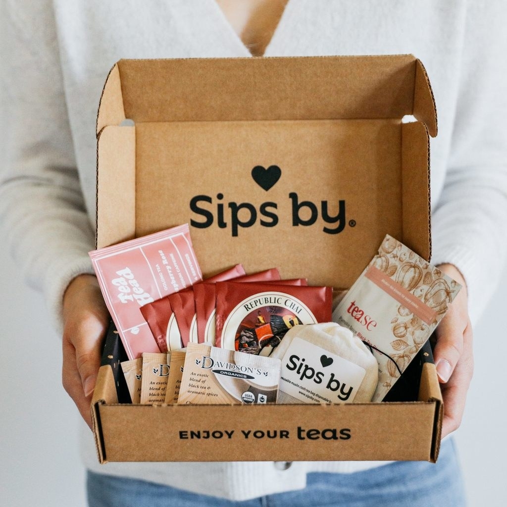 model holding sips by box full of five kinds of tea bags and loose leaf tea