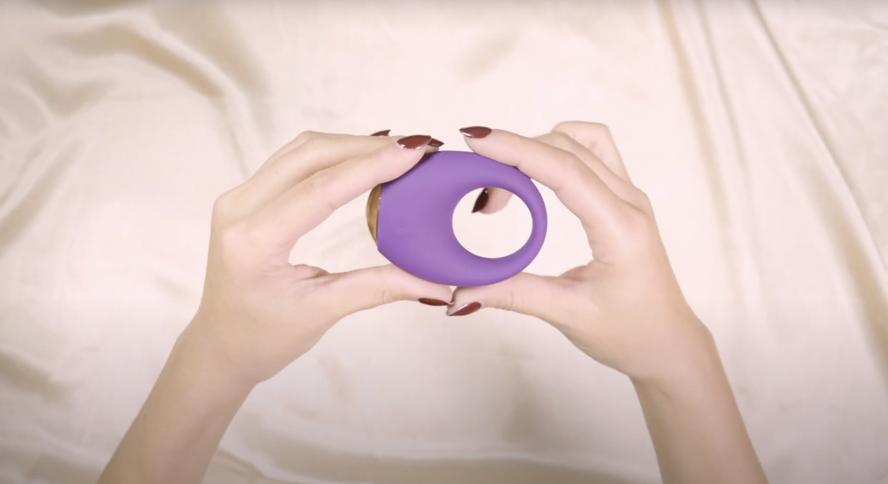 A model holding the purple and gold cock ring and demonstrating its flexibility