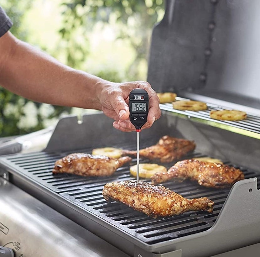 A person probing a chicken leg on the BBQ to check its temperature 