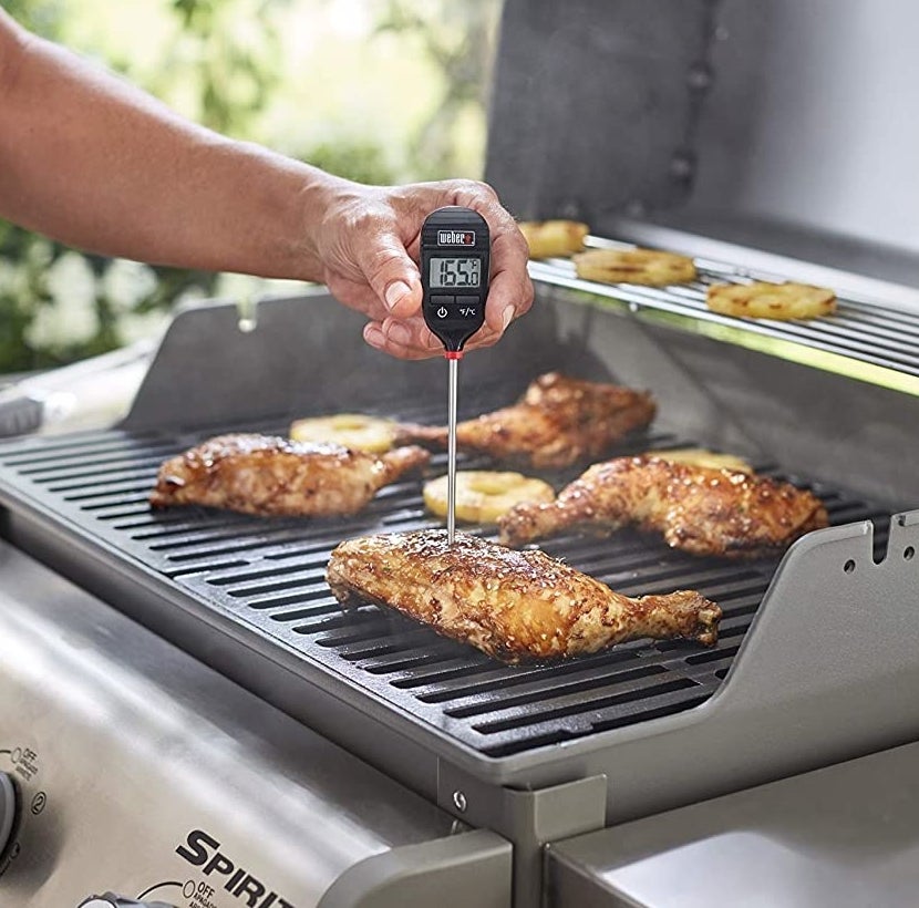 A person probing a chicken leg on the BBQ to check its temperature