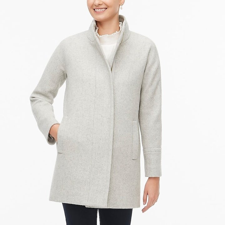 model wearing light grey zip-up coat that hits just below hips; their hand is in the pocket