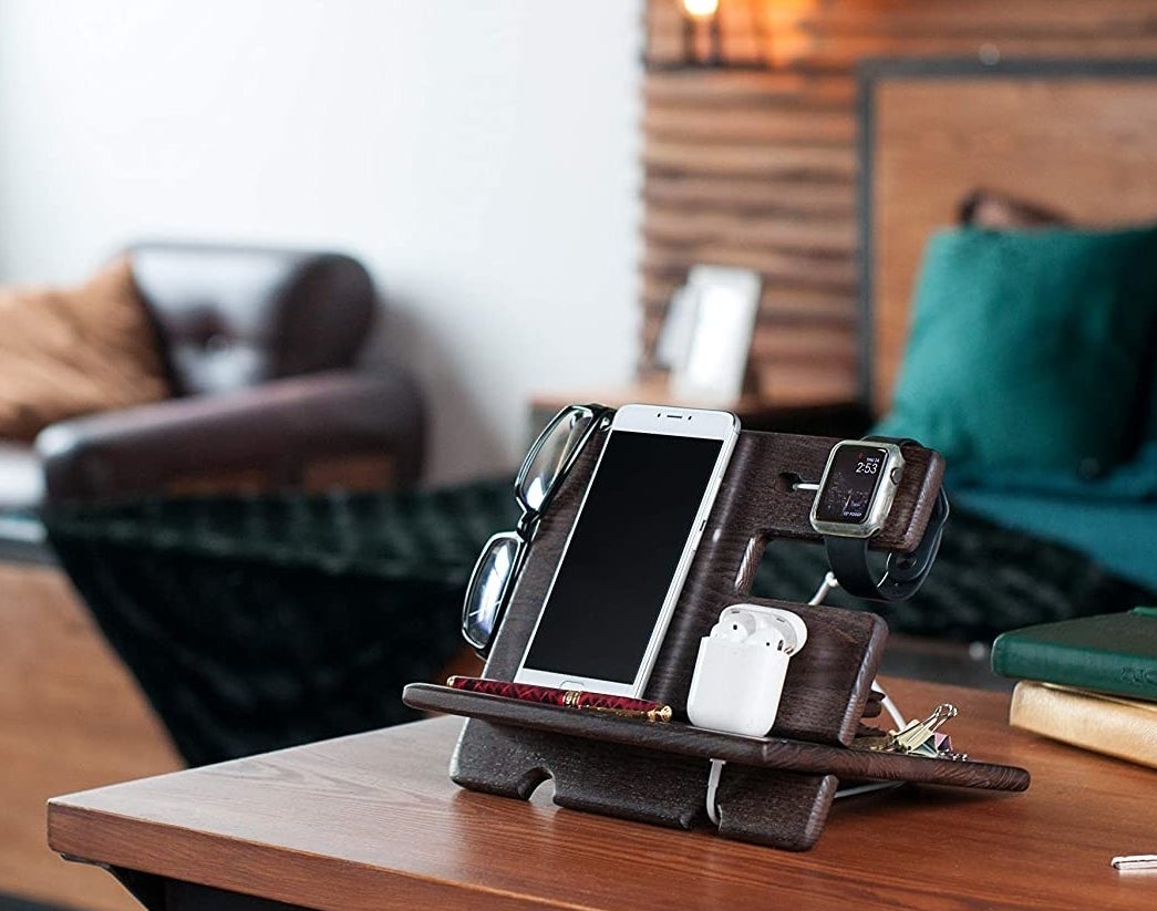 A docking station on a table holding a pair of glasses, a phone, earphones, and keys