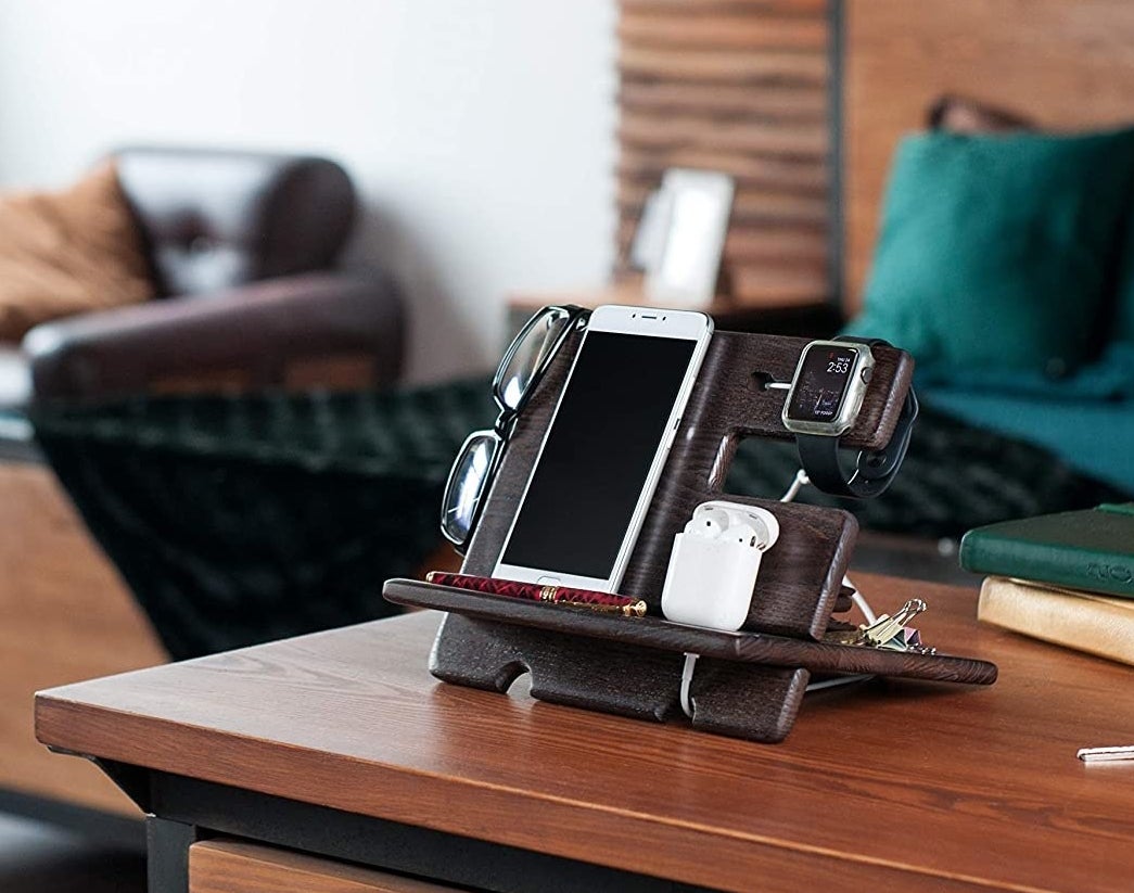 A docking station on a table holding a pair of glasses, a phone, earphones, and keys