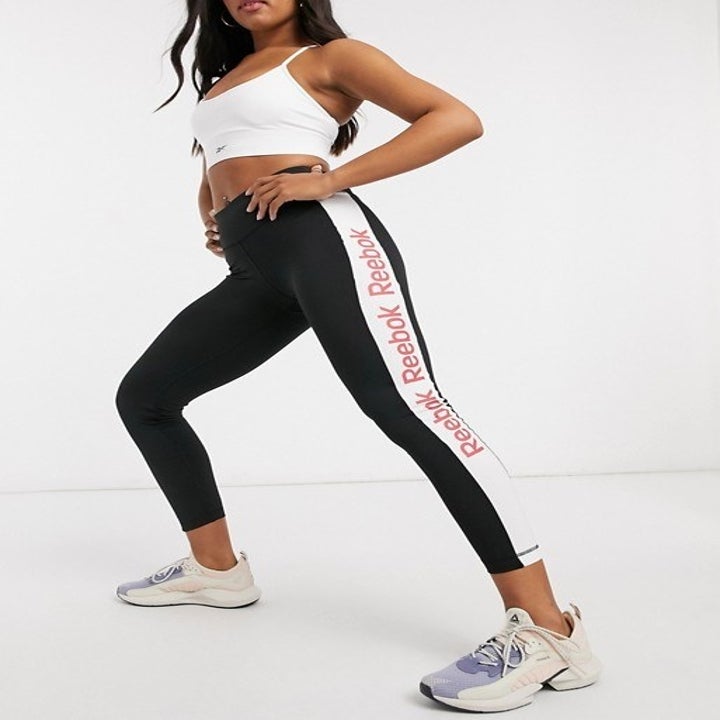 Model in black workout leggings with white stripe up the side that says "Reebok" in red three times