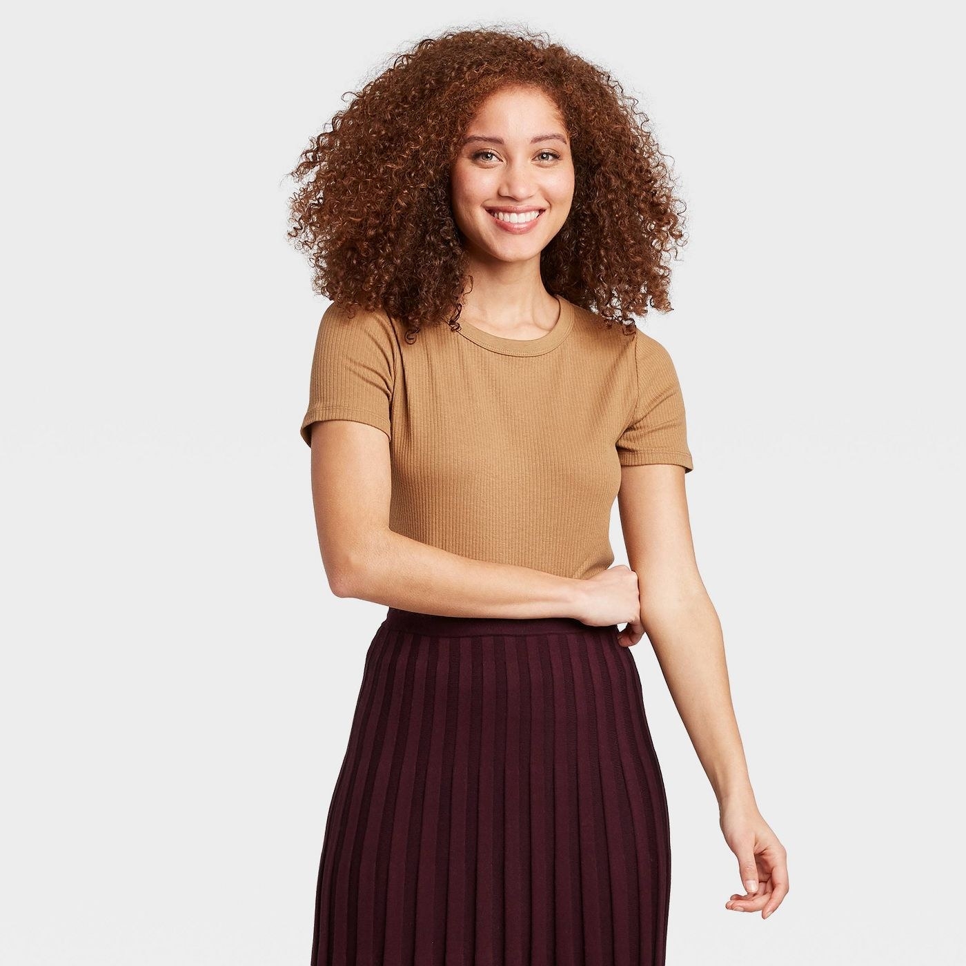 A smiling person wearing the t-shirt in brown and a brown skirt