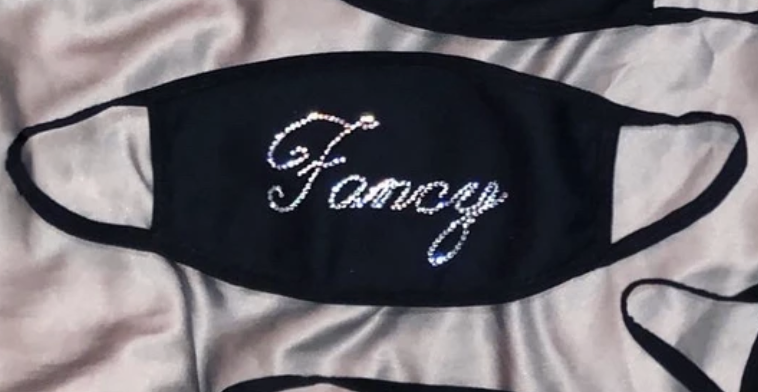 A black face mask with bedazzled message that says "fancy"