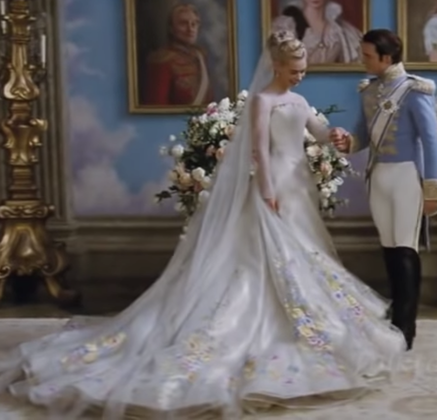 Cinderella in a satin ballgown with a long train that has embroidered flowers on it and a high square neck strapless top with sheer sleeves under it