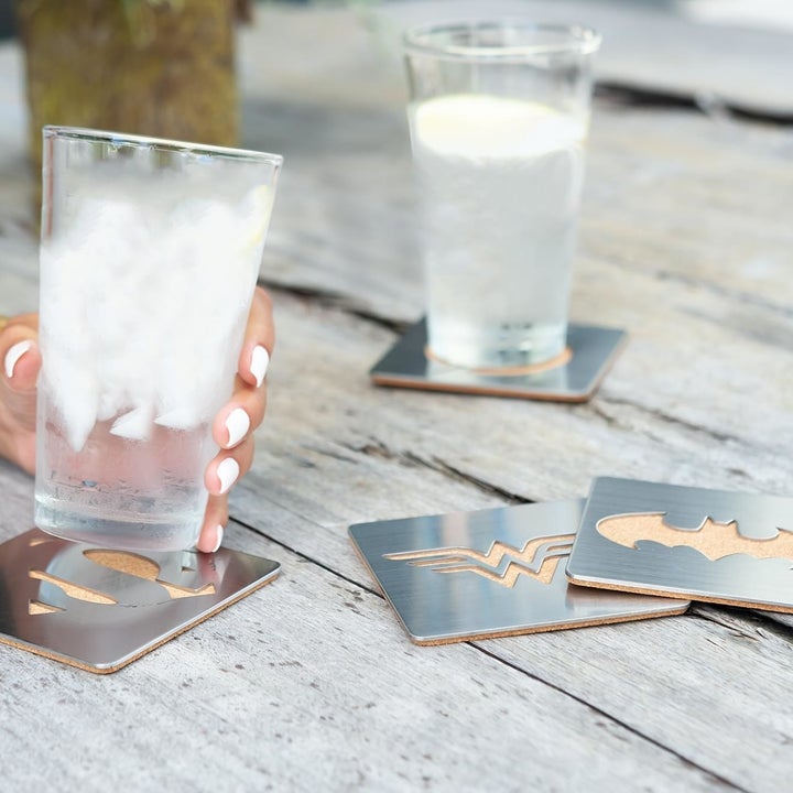 four stainless steel coasters each with a super hero logo: one for superman, wonder woman, batman, and the flash 
