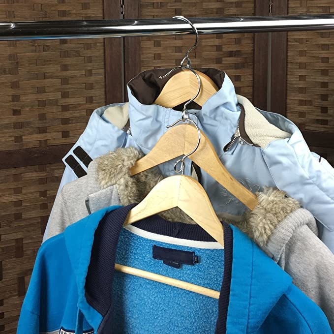 Three coats on wooden hangers that are hanging vertically off of a metal bar 