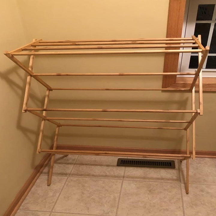 A reviewer photo of the bamboo wood drying rack with  three levels or bars to hang clothes on 