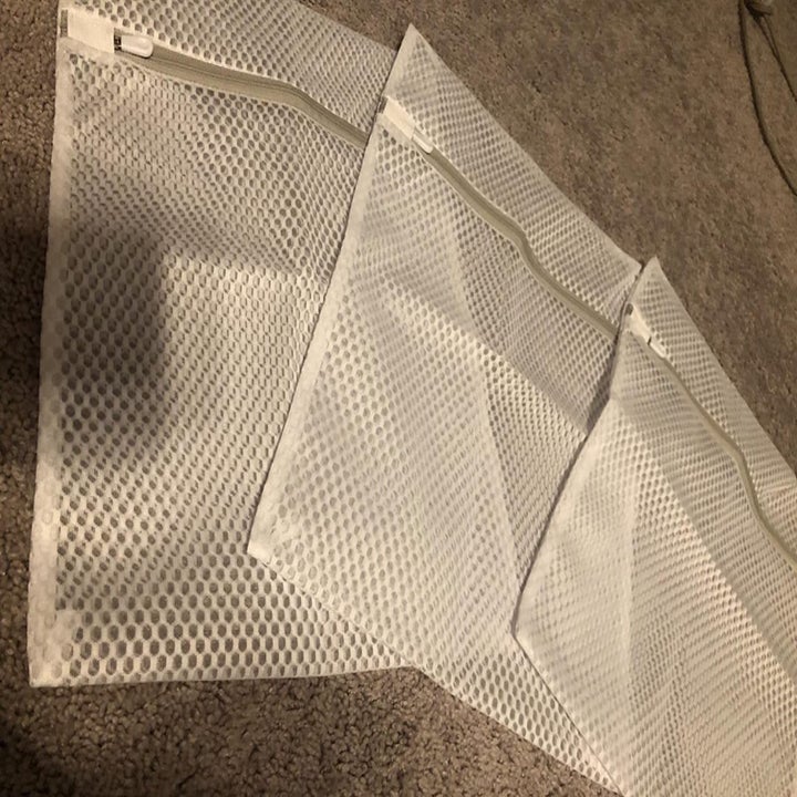 A reviewer photo of three mesh laundry bags with zip closures laid out on the carpet 