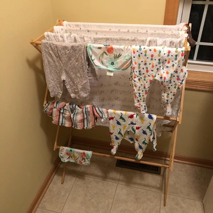 A reviewer photo of the same dry rack with lots of clothes hanging on the rack 
