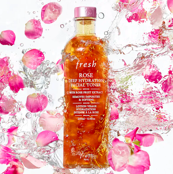 Bottle of Fresh Rose Deep Hydration Facial Toner with rose petals and a clear formula inside in a backdrop of pink roses