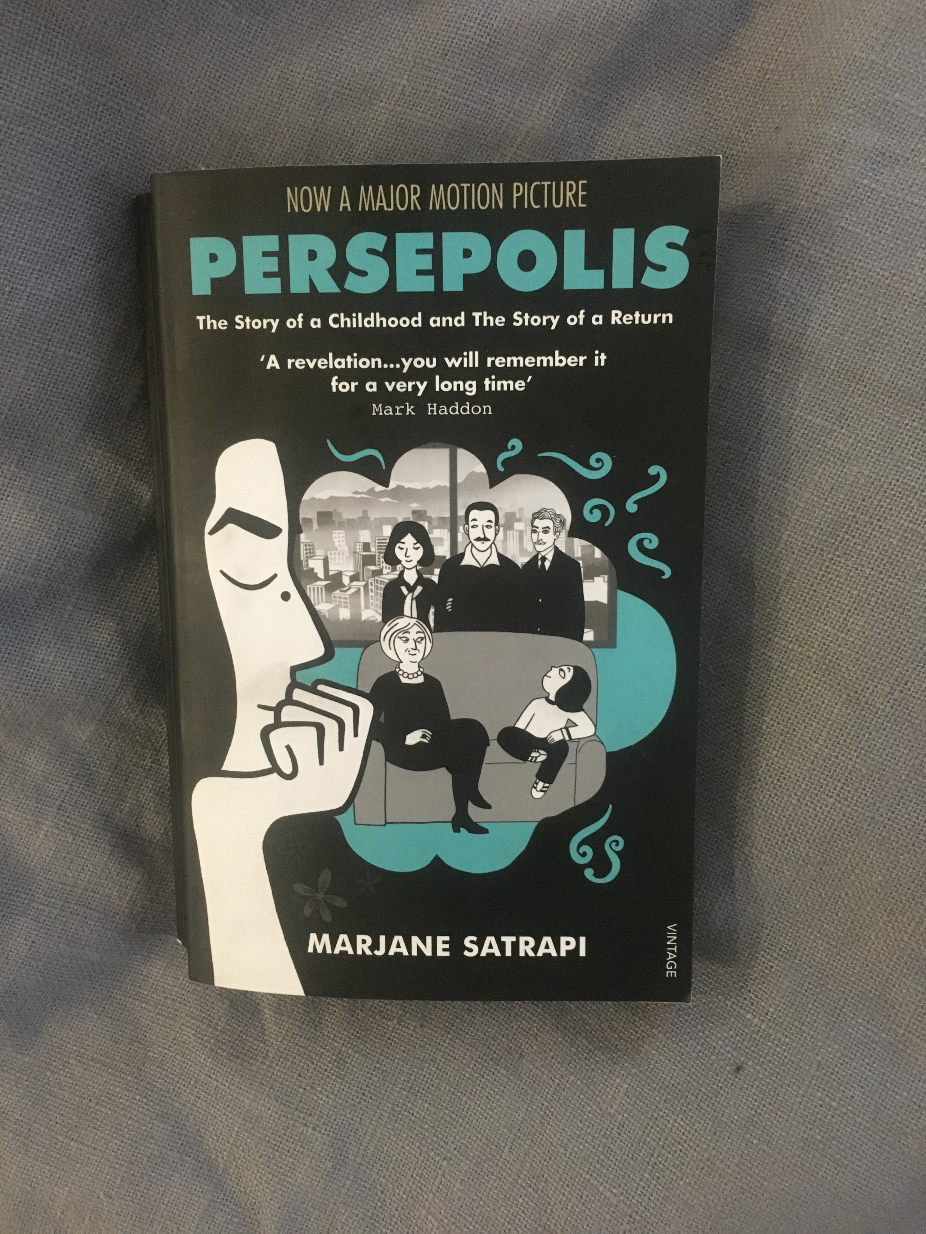 A graphic novel with the front cover showing a profile view of a person and a family sitting around a couch with a city showing in the window behind them