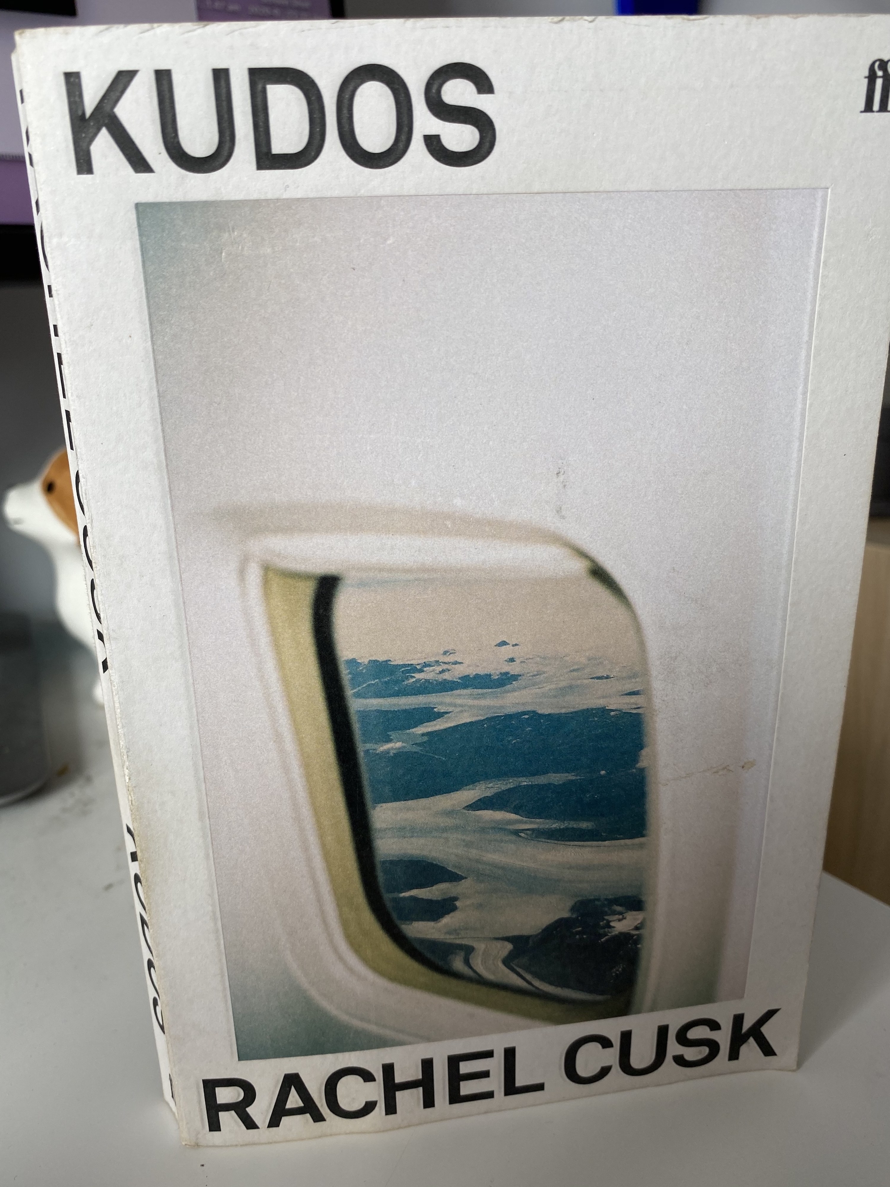 Cover shows an aeroplane window with a mountain view below