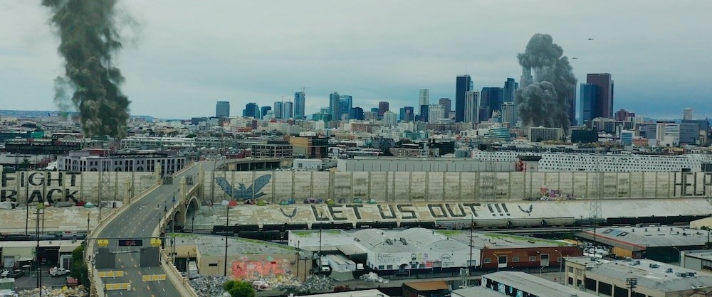 A shot from the film shows smoke in the sky over Los Angeles, with a fence built around the city, and graffiti that says &quot;Let us out&quot;