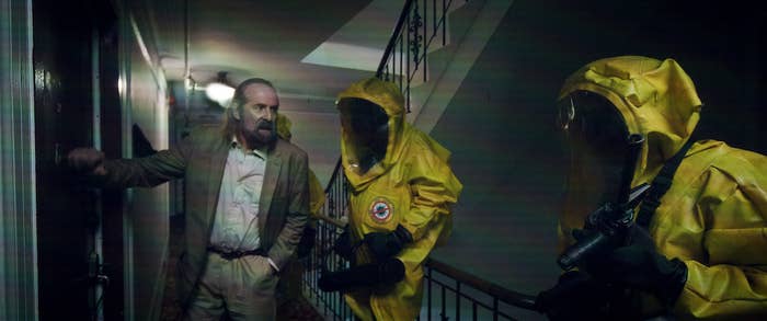 A shot from the film shows a plainclothes man with people in hazmat suits in a hallway