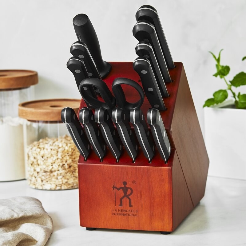 A knife block set with lots of knives with black handles and kitchen sheers on a white kitchen counter top 