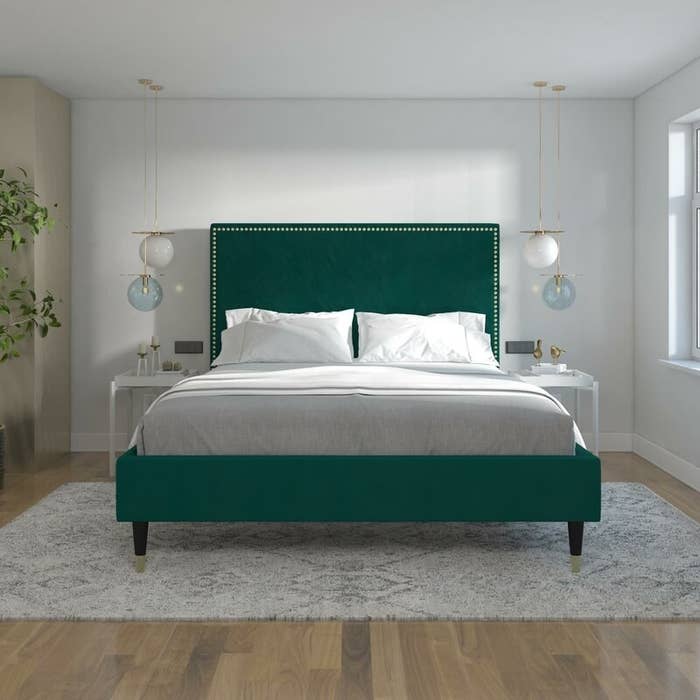 Green velvet platform bed with gray and white sheets in a bright bedroom