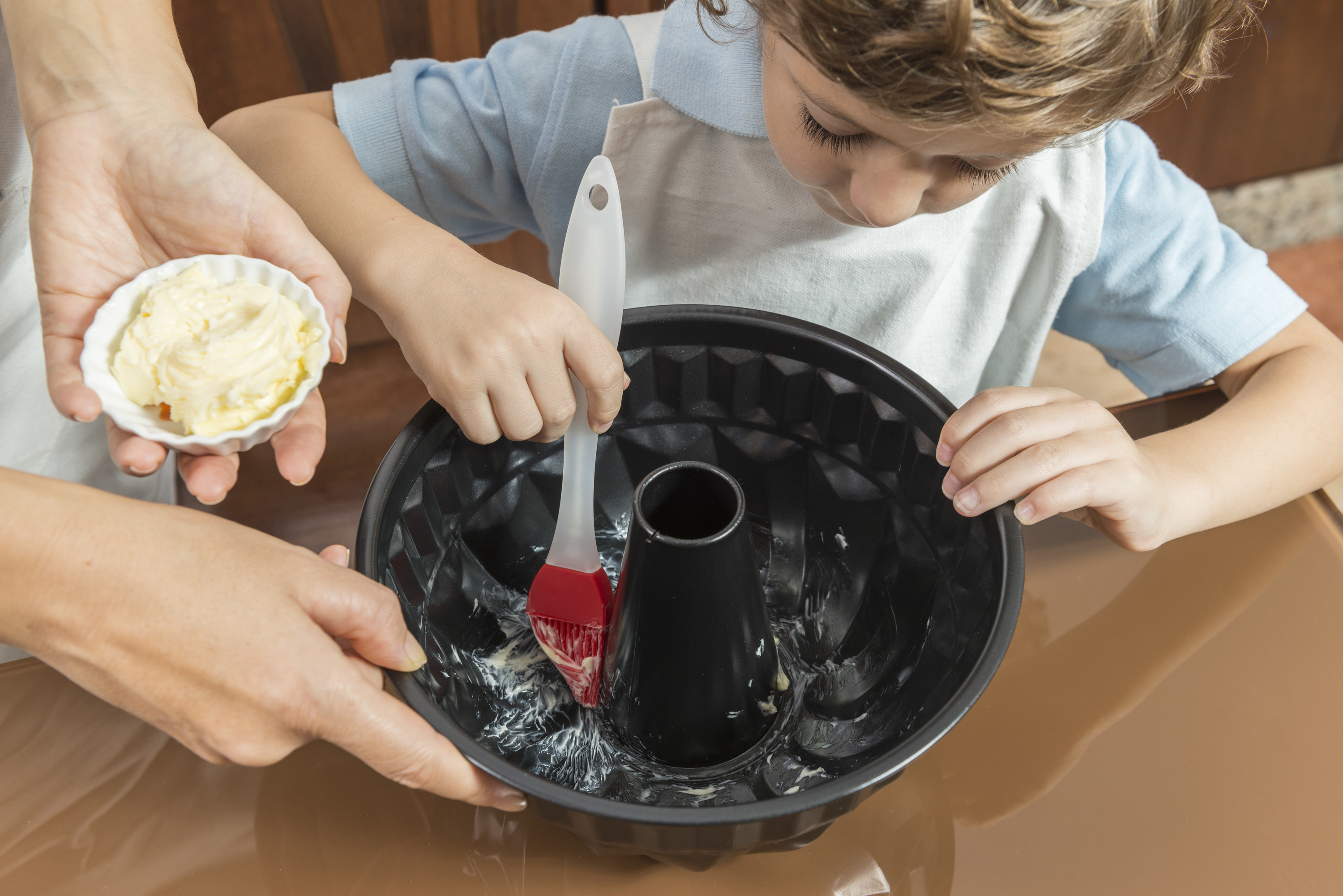 Child spreading butter at the bottom of a bundt cake pan