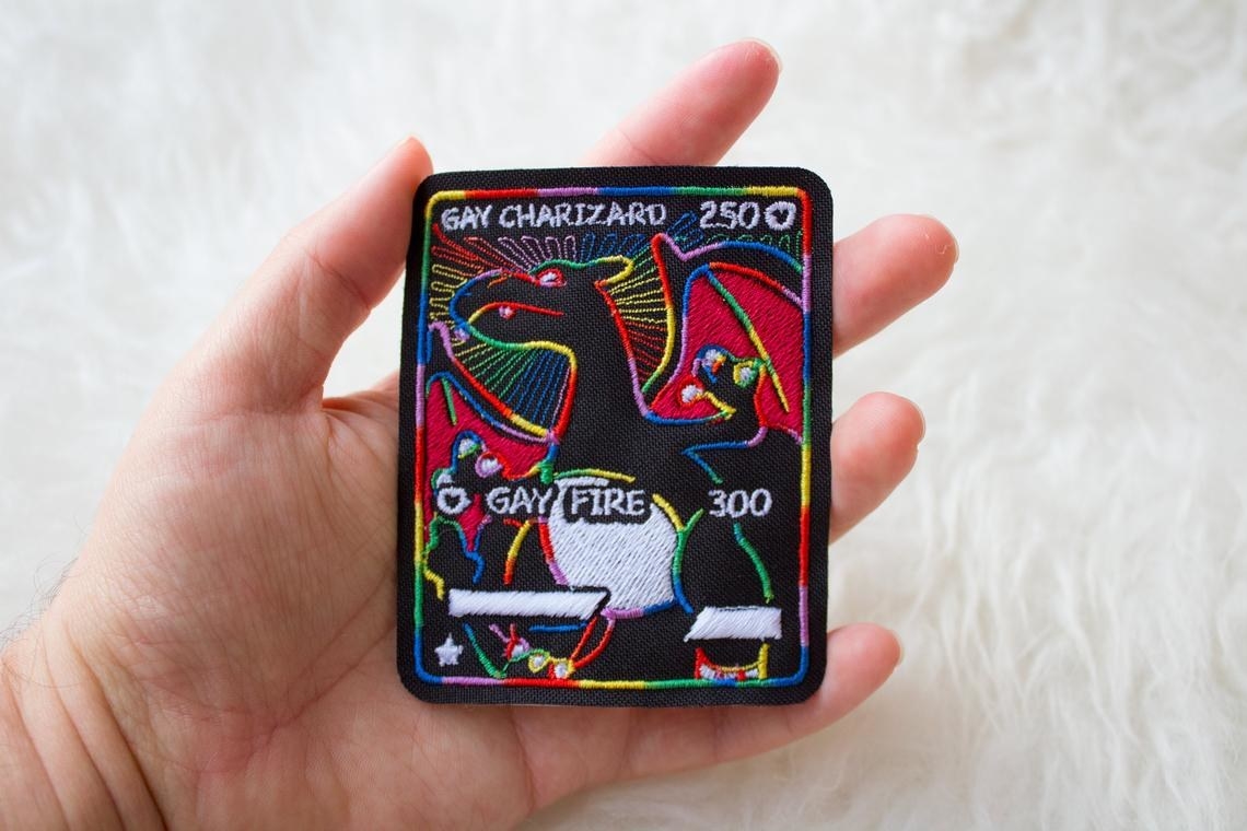 black patch with rainbow outlined charizard card that says gay charizard with the move gay fire