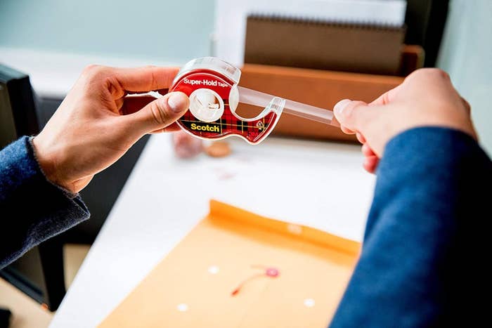 Model's hands holding Scotch Magic Tape dispenser and pulling off a piece of clear tape